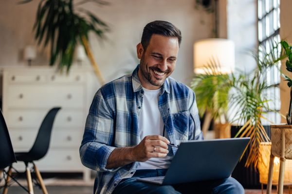 Happy man using a laptop, being at the office, holding his glass