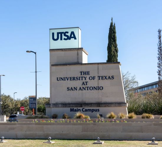 A sign for the University of Texas at San Antonio Main Campus stands proudly, surrounded by trees and shrubs, not far from the comfort of Elm Hollow Apartments.