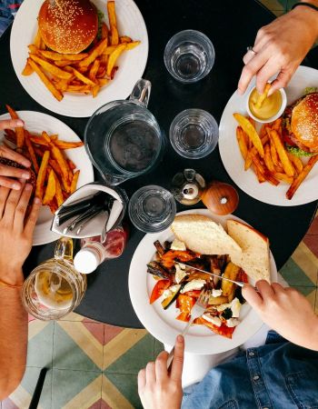 At Elm Hollow Apartments, four people enjoy burgers and fries at a round table, surrounded by drinks and condiments, seen from above.